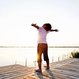 Young boy with his arms stretched wide standing on a dock in the sunlight
