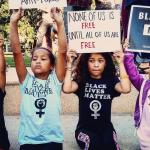 Photograph of African American and white children holding protest signs that read "Black Lives Matter" and "None of Us is Free until All of Us are Free"