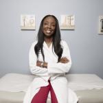 Photograph of Dr. Nadine Burke Harris, an African American woman seated in a white lab coat on an examining table in a doctor's office