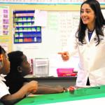 Photograph of woman physician visiting a classroom with young Black students looking up at her