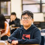 Photo of Latino adolescent boy sitting at his desk in a classroom wearing glasses