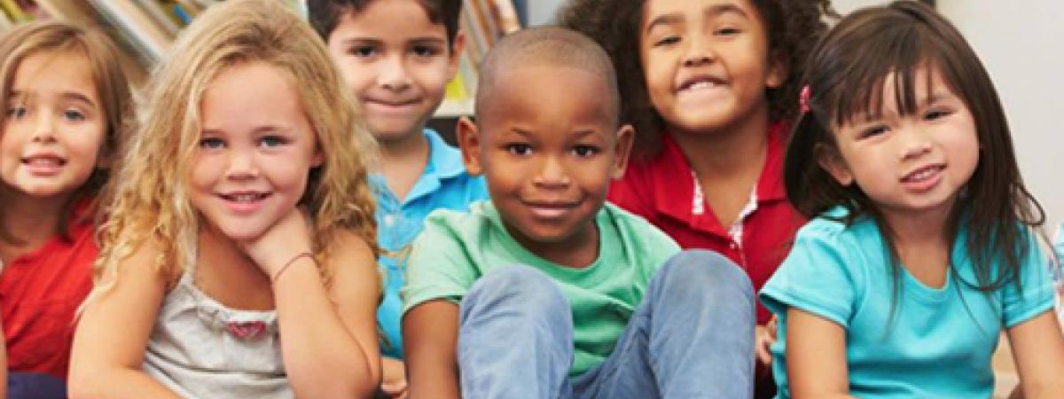 Photo of young children of various racial and gender identities smiling at the camera