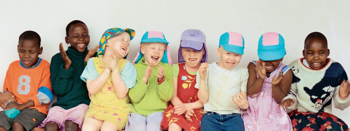 Photograph of children sitting on a bench laughing - some are Black and some have light skin due to albinism