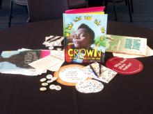 Table of books, buttons, and event papers surrounded by a book titled Crown placed in the center