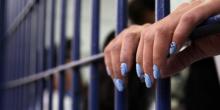 Photograph of hands with manicured nails holding on to prison cell bars