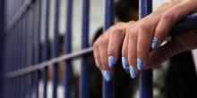 Photograph of hands with manicured nails holding on to prison cell bars