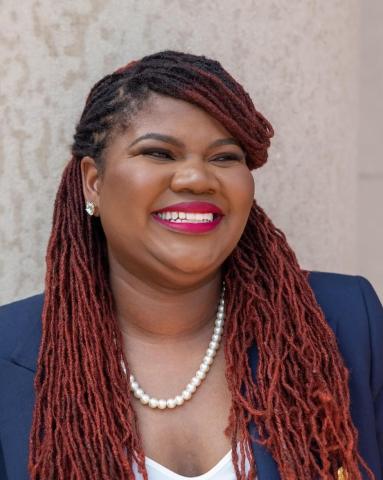 Kellie Carter Jackson in a blue blazer with white blouse underneath. Her braids swoop over the left side of her face, with the length resting on either side of her shoulders