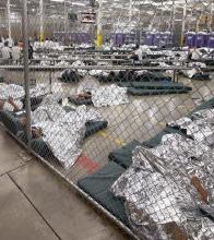 Photograph of immigrant detention center with wire fence and children sleeping on the floor