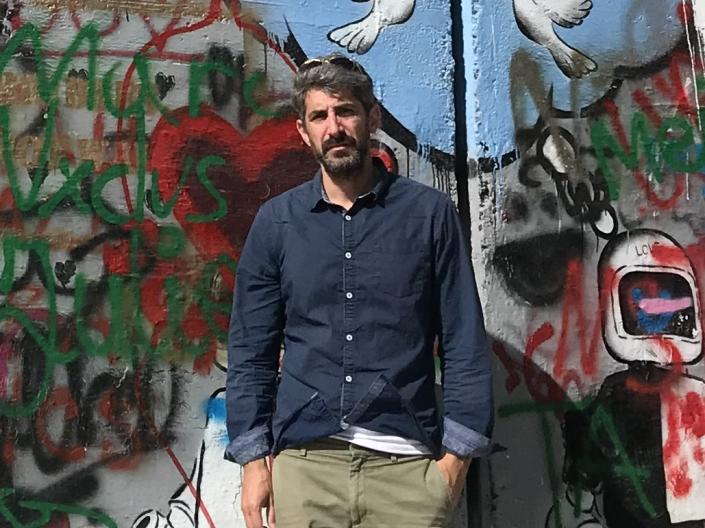 Photograph of Professor Avi Cover standing in front of the wall with grafitti between Israel and Gaza