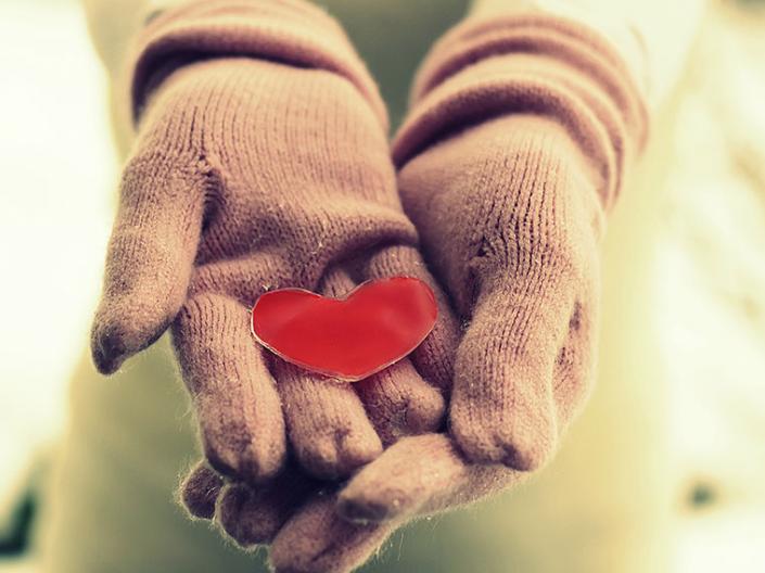 A red heart cutout held in gloved hands.