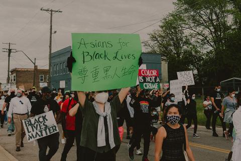 protest with multiple signs held up focus on sign reading Asians for Black Lives