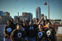 group of young people in matching brown shirts standing smiling at camera in front of city skyline