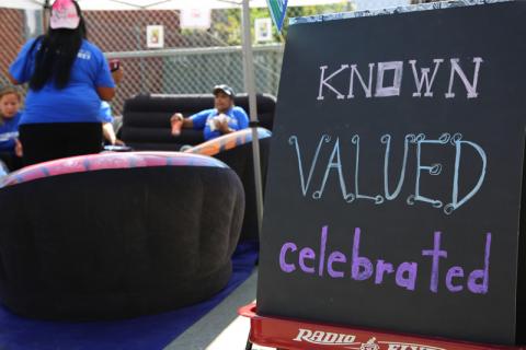 Large sign that reads Known Valued celebrate in front of four women talking in a circle