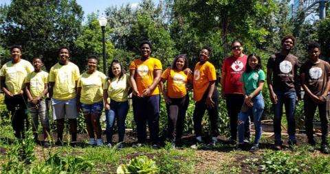 Group of teens standing together in community garden facing camera smiling