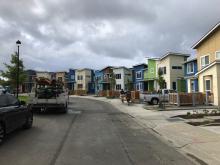 Group of houses, workers walking down sidewalk carrying wood. Construction truck parked in street.