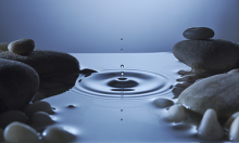 A raindrop in a still pool causing a rippling wave.