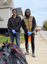 Two men outdoors standing in front of bags of trash