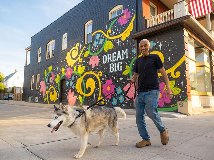 man walking dog in front of mural on wall that says Dream Big