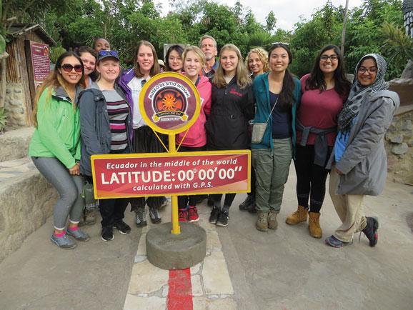 group of students standing in front of sign that reads "Ecuador in the middle of the world"