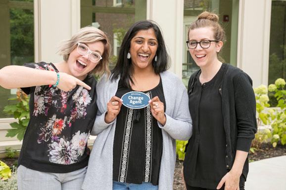 three students holding change agent stickers smiling at camera