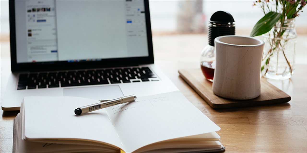 Open notebook with a pen on it in front of a laptop