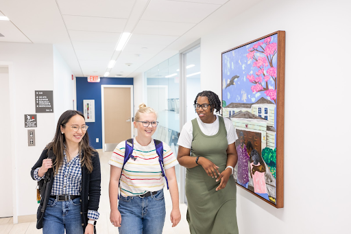 Three female presenting students walking down hallway
