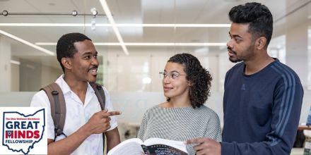 Three students talking over an open books with Great Minds Fellowship logo in the bottom left corner