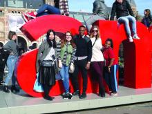 Image of five students standing in front of a large red lowercase letter A and large lowercase letter N, with three students sitting above