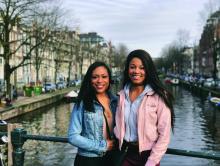 Image of two students on a bridge overlooking a canal with buildings and boats on both sides