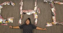 Young woman laying on her back on the floor. Above her are the letter CHI made from bags.
