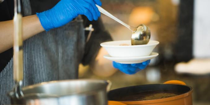 Person with blue latex gloves on ladeling soup into a bowl