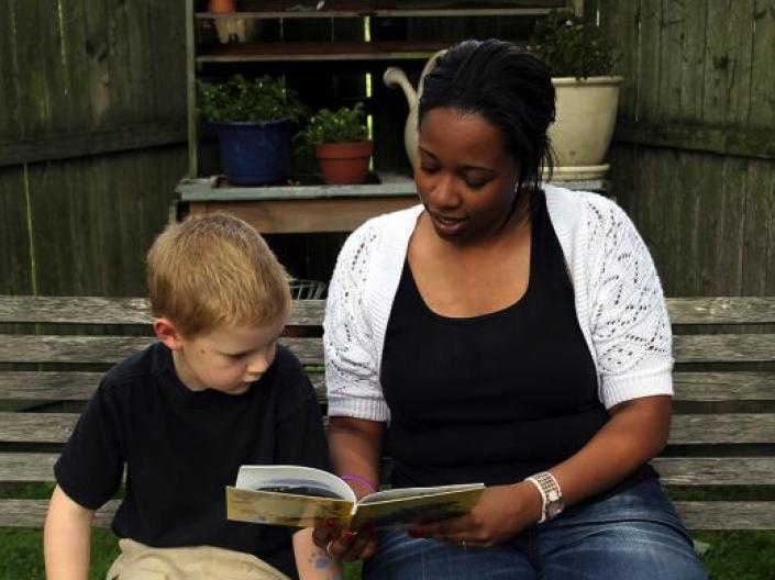 Mandel student sitting on bench with a young boy reading a book