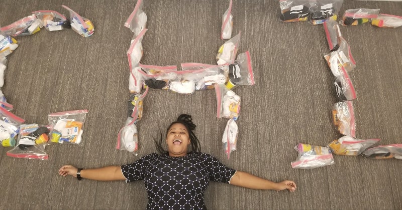Young woman laying on her back on the floor. Above her are the letter CHI made from bags.