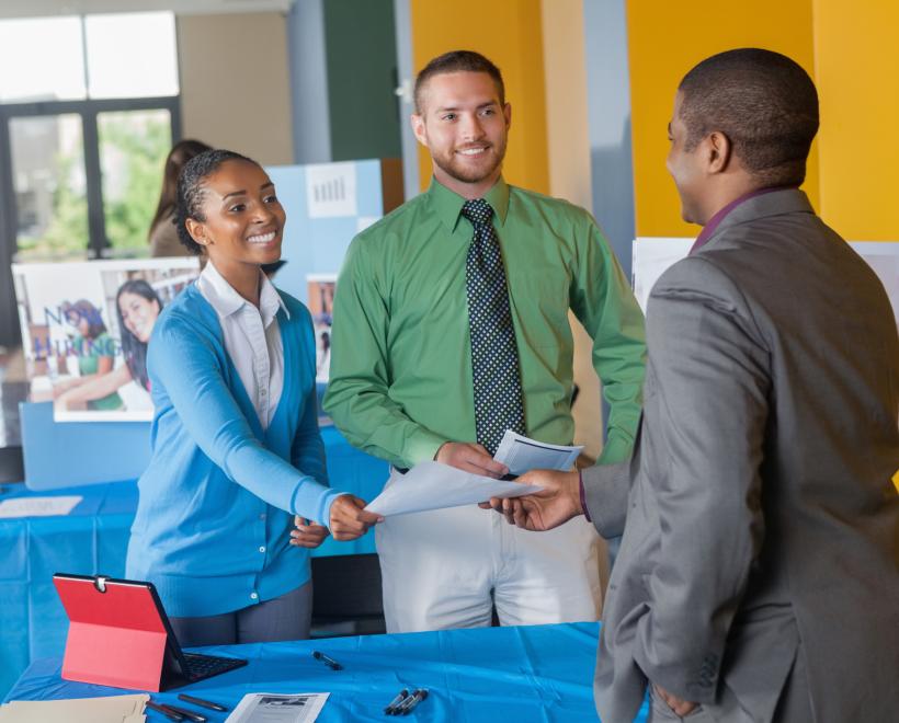 Students shake hands with an employer at a job fair table