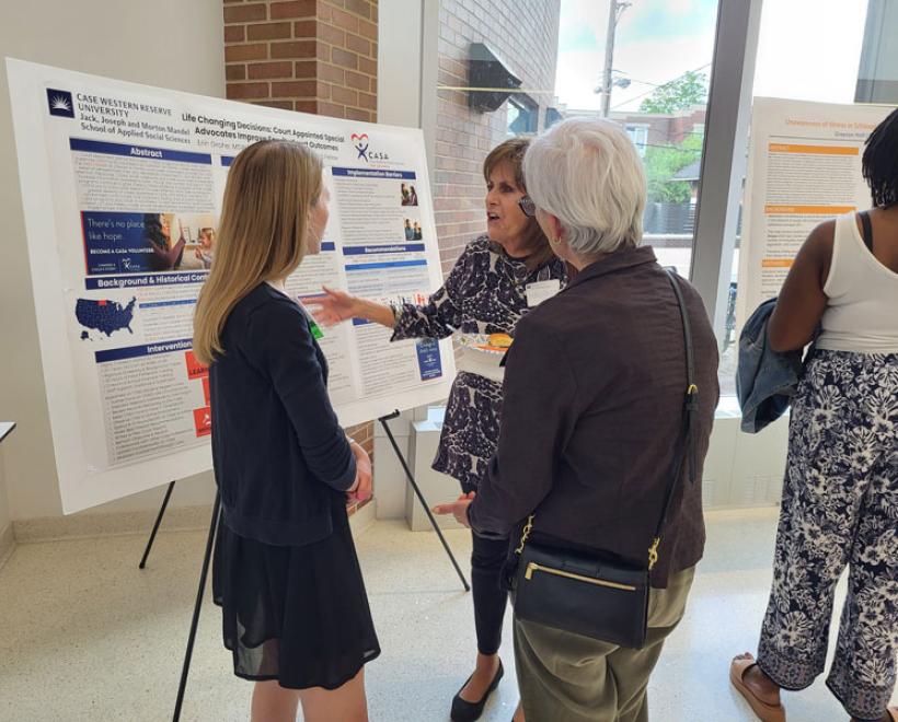 A student presents her poster presentation to two people