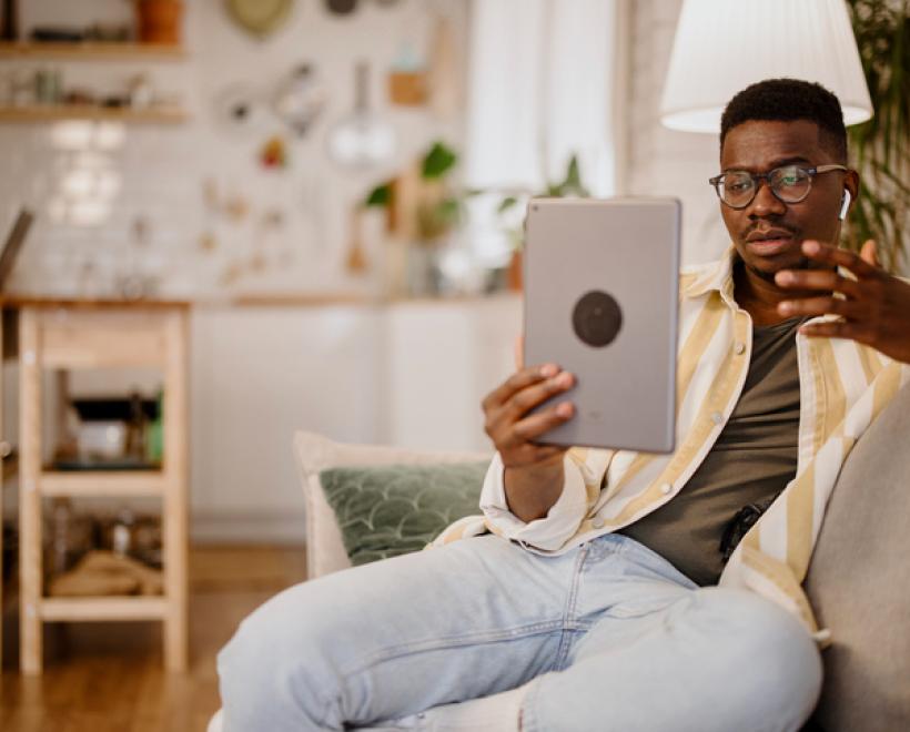 Man sitting in a chair holding a tablet and talking with his hand
