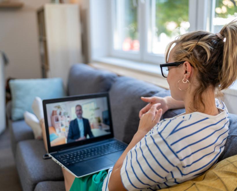 Woman sits on her couch looking at a man on a laptop