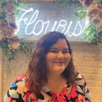 Jasmine Myers in front of a neon "Flourish" sign