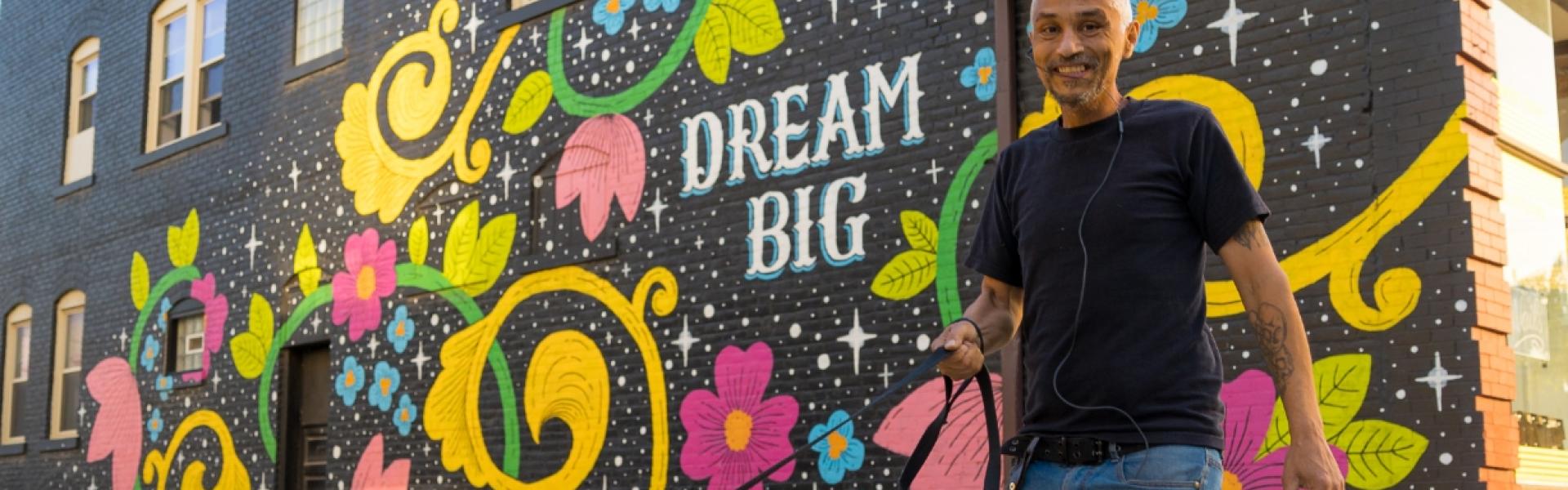 Male walking his dog in front of the Big Dream mural
