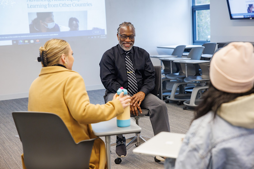 Male presenting professor sitting in classroom with students