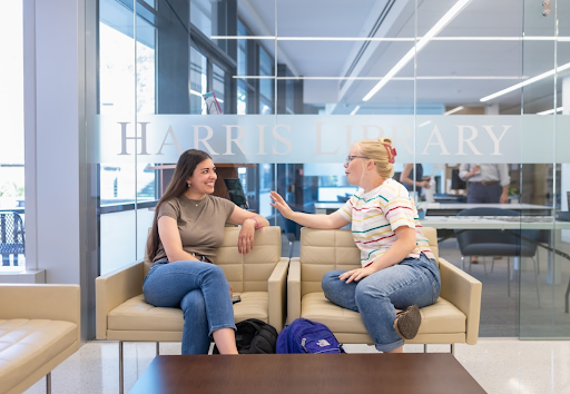 Two students sitting in front of glass wall reading Harris Library