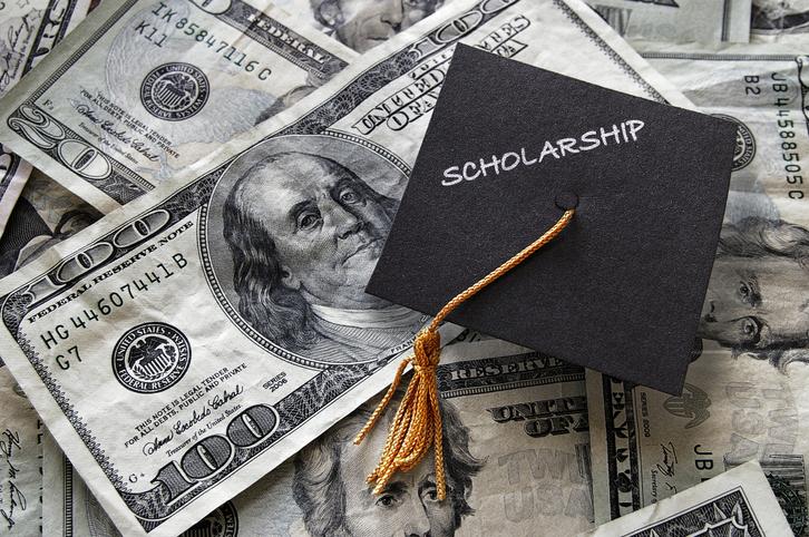 Mortar board cap with "Scholarship" written on it placed on top of $100 bills