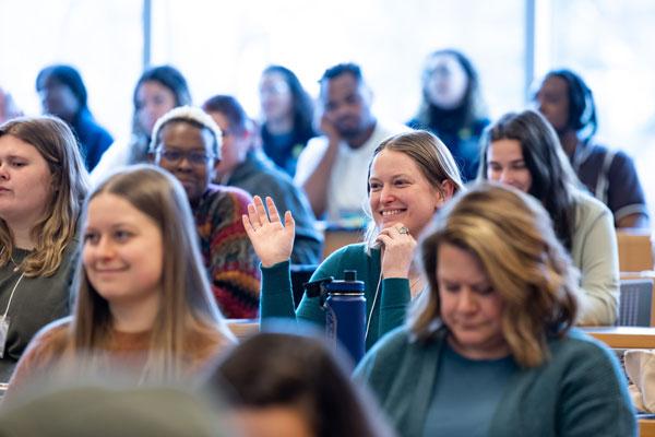 Students in auditorium classroom smiling and one person raising their hand