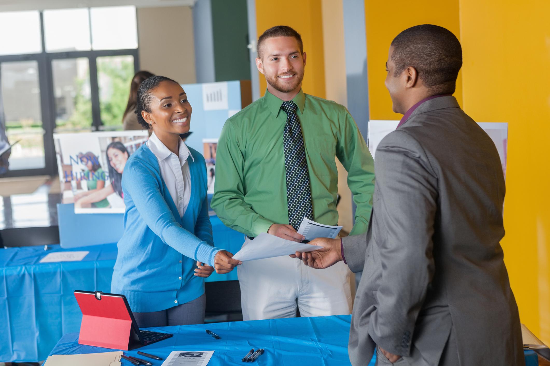 Students shake hands with an employer at a job fair table