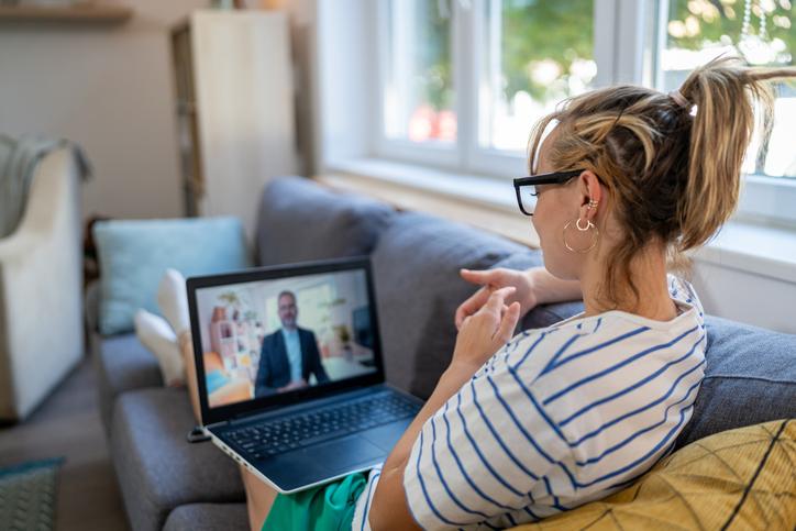 Woman sits on her couch looking at a man on a laptop