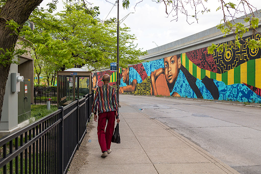 Person walking down a street, colorful mural on right