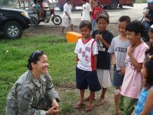 Janette Kautzman in her Army uniform squatting and talking to children