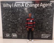 Ayowole Ajiboye in front of Mandel School Change Agent blackboard sign