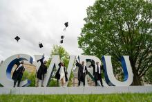 Graduates throw their caps in the air in front of the CWRU block letters