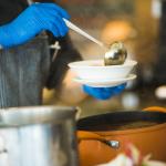 Person with blue latex gloves on ladeling soup into a bowl